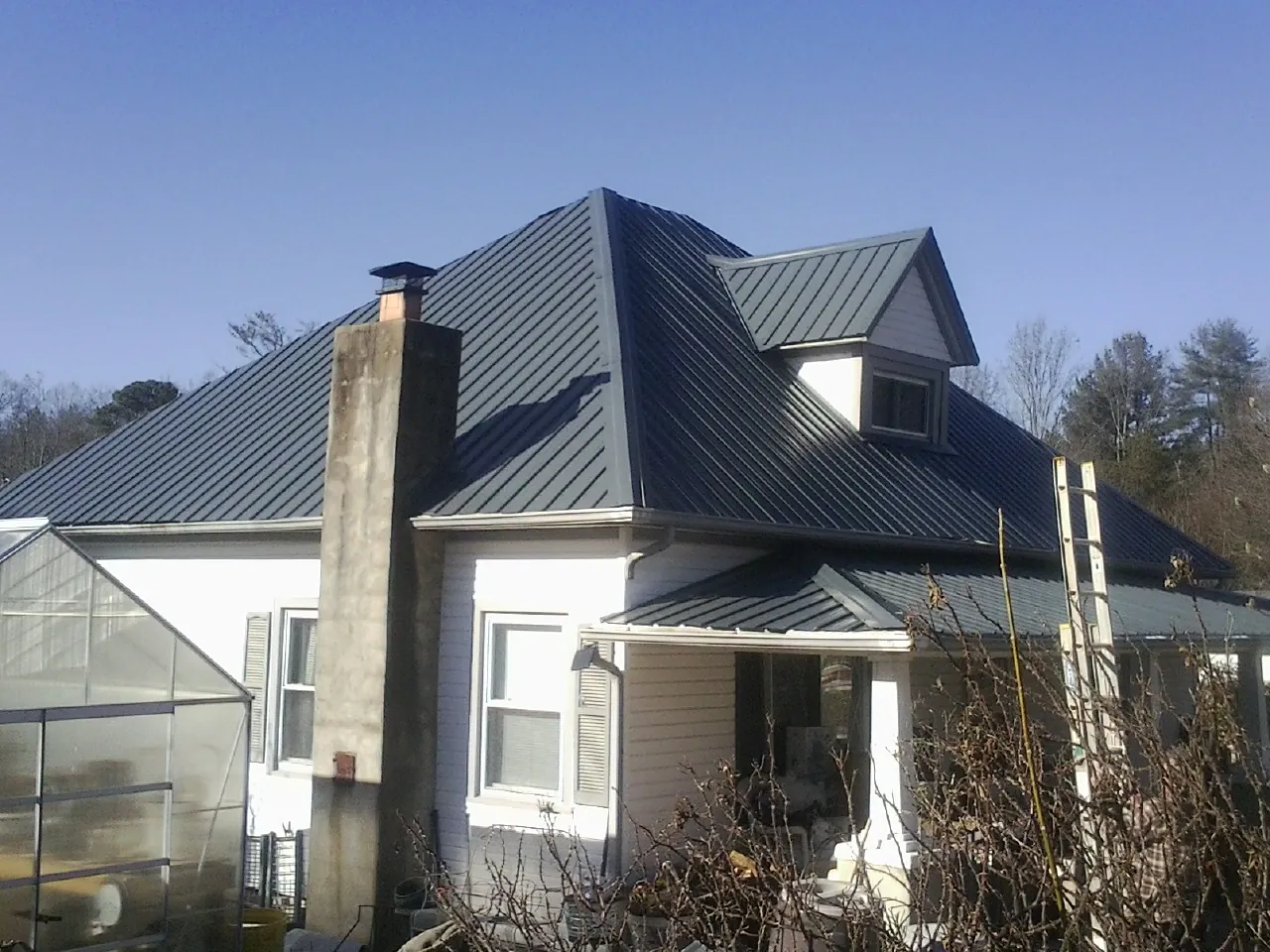 Dark blue standing seam metal roof on a white farmhouse with dormer — Slate & Tile Roof Repair by Roofing Brothers in Chapman Ranch