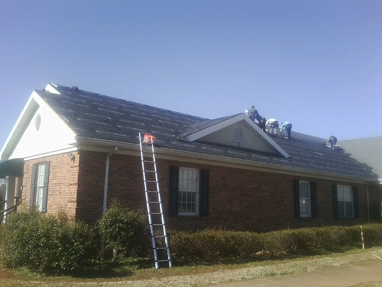 Crew tearing shingles off a brick ranch roof with a ladder set — Emergency Roof Repair work by our crew in Chapman Ranch