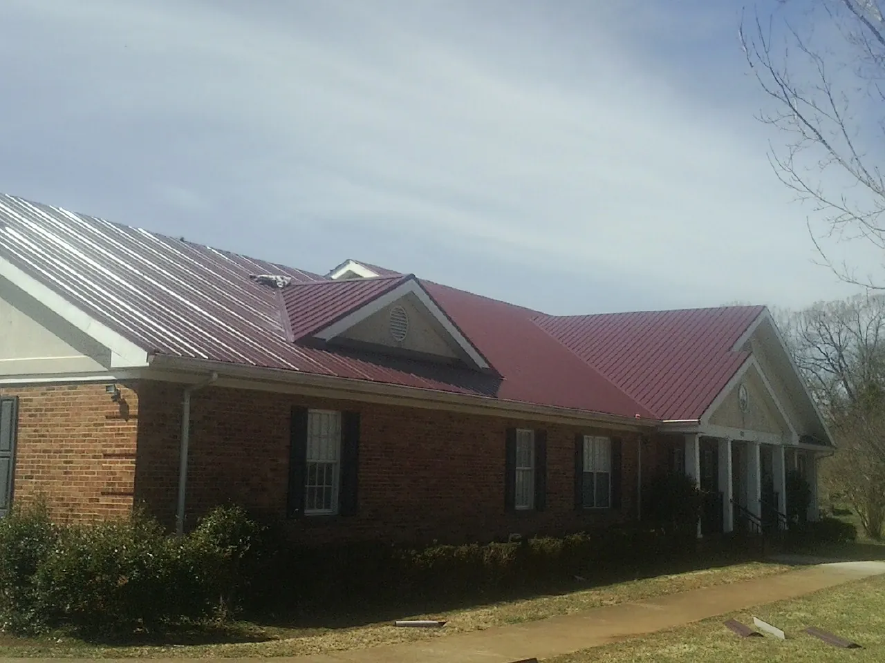 Red metal roof with gabled entries on a long brick building, from a Hail Damage Roof Repair job in Chapman Ranch
