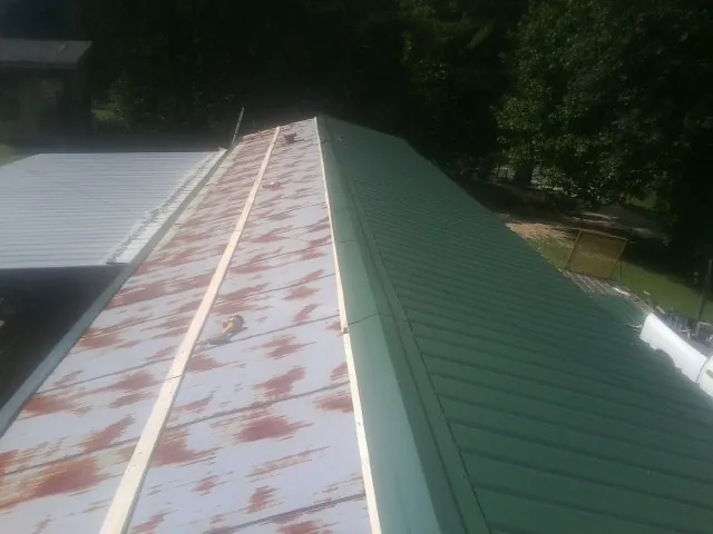 Old rusted panels beside newly installed green metal roofing — Wind Damage Roof Repair by Roofing Brothers in Chapman Ranch