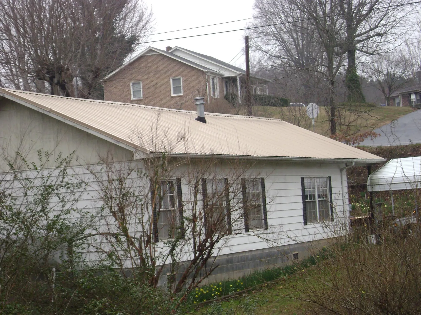Tan metal roof on a white sided house set into a hillside — Commercial Roofing by Roofing Brothers in Chapman Ranch