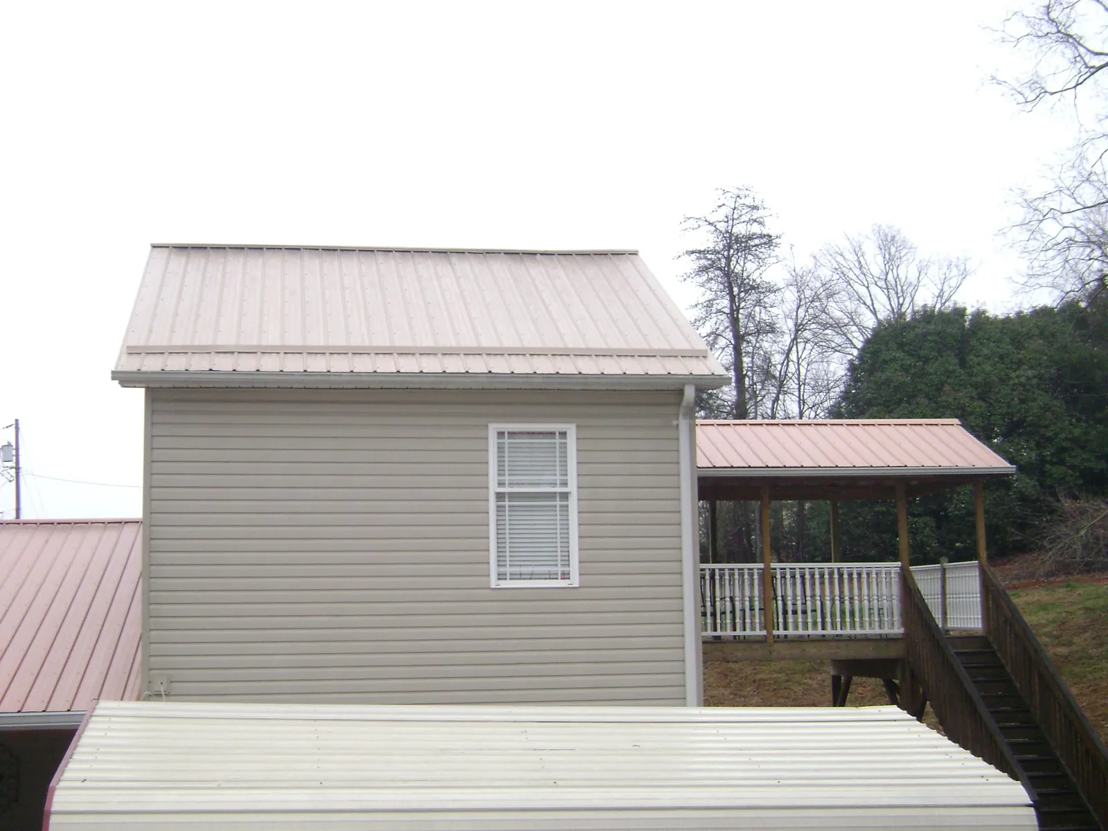 Tan metal roofs on a two story addition and attached porch, from a Roof Replacement job in Chapman Ranch
